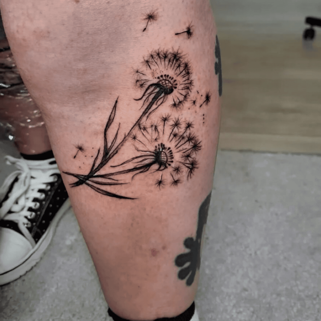 Dandelion tattoo on leg with seeds blowing.