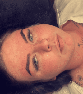 Person with tattoos lying down, looking thoughtful.