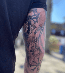 Arm with Viking-themed tattoos in sunlight.