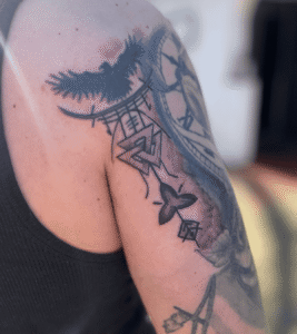 Close-up of tattooed arm with clock and bird design.